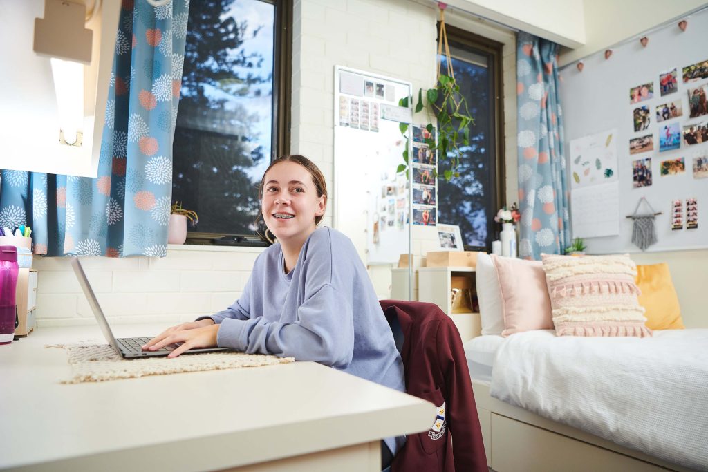 A happy girl is seated at a desk in her dorm room at St Mary's Anglican Girls School.