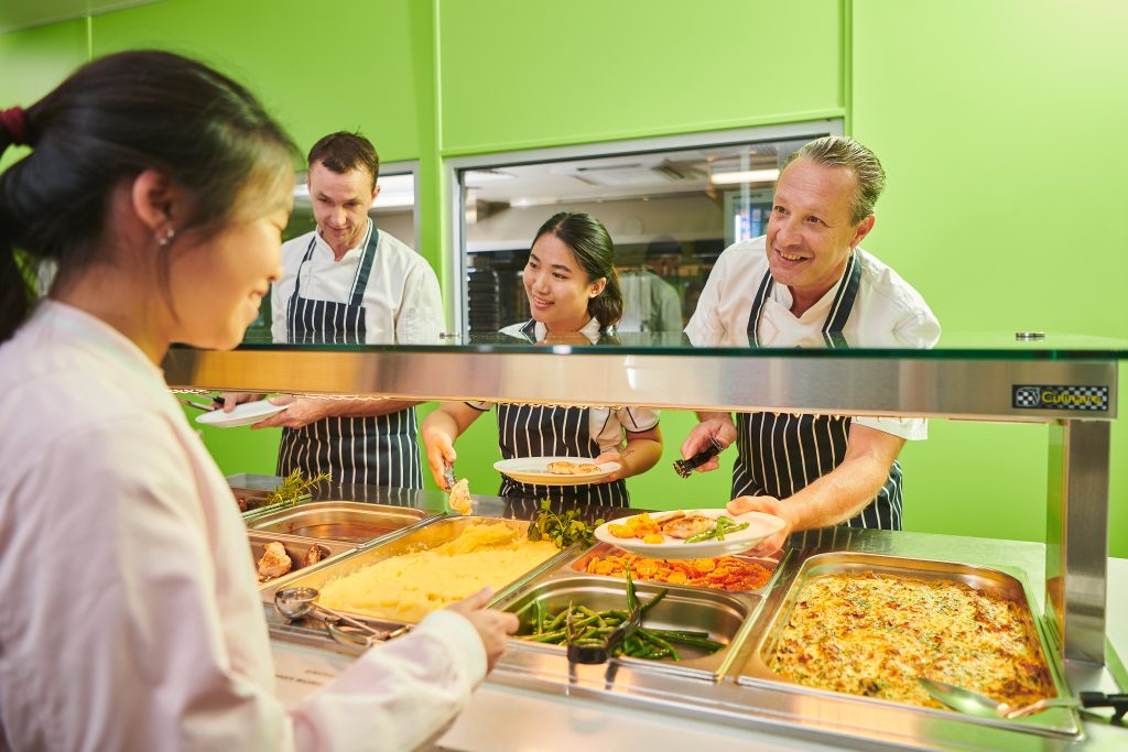 In a restaurant at St Mary's Girl's boarding School, a team of individuals serves a delicious range of hot and cold dinner options to a group of people.