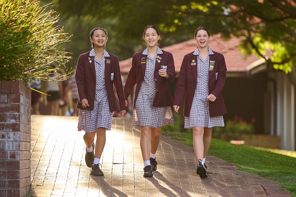 Three girls in school uniforms walking down a brick path at St Mary's Anglican Girls School.